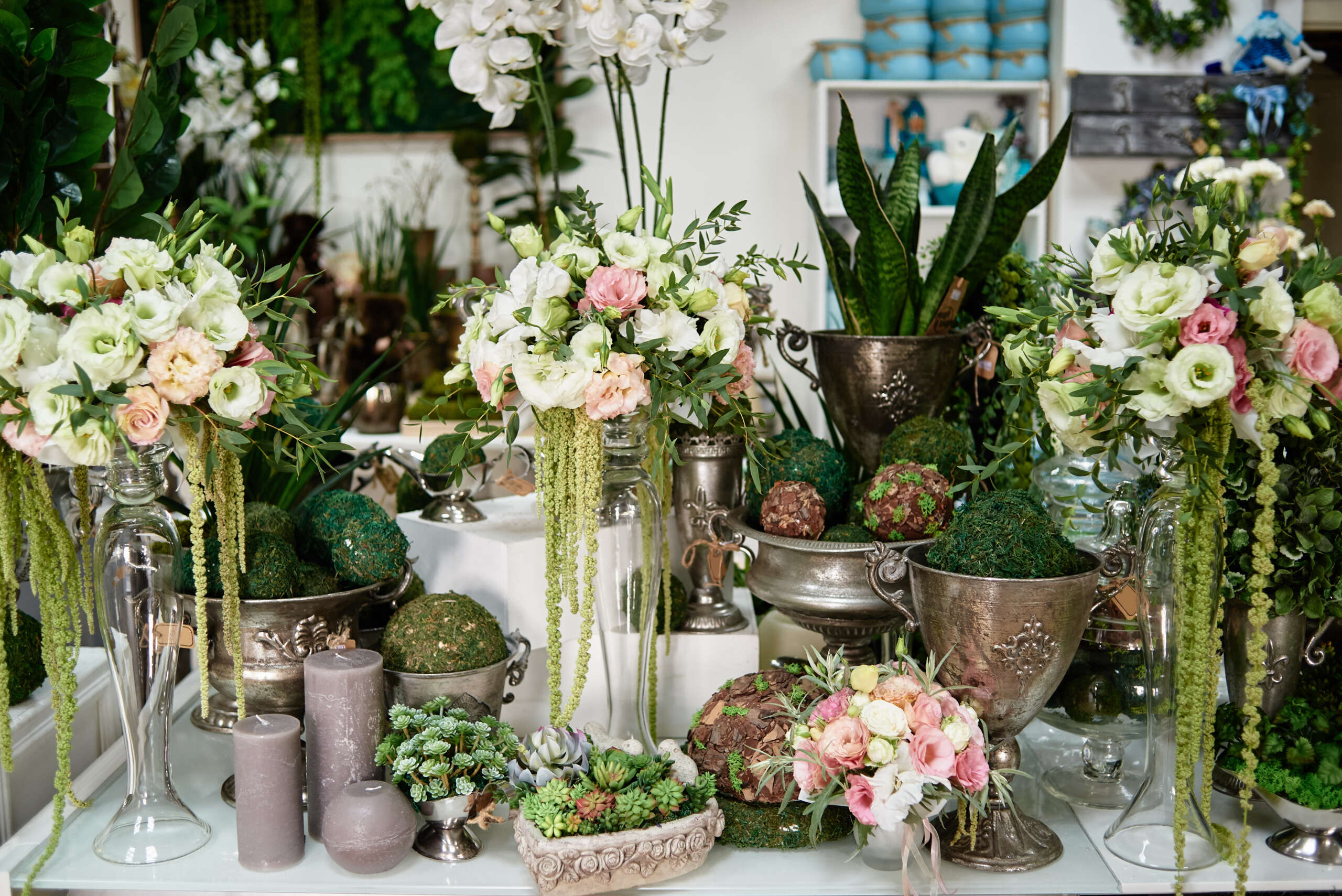 Many flowers and candles on table in florist shop, copy space. Small business. Floral design studio, luxury wedding decorations. Flowers delivery. Holiday and floristry concept